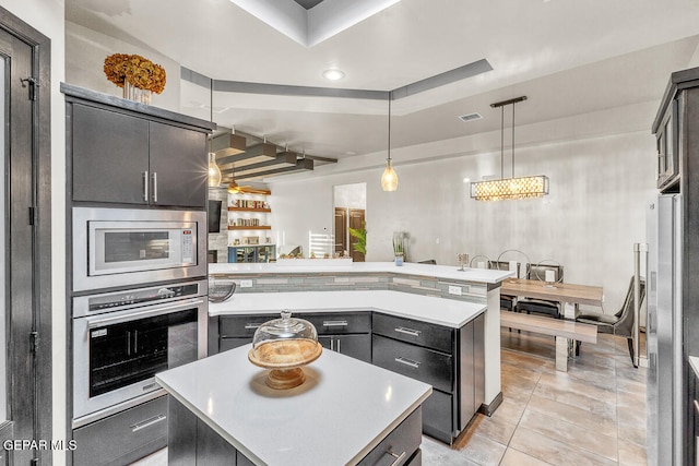 kitchen with a tray ceiling, decorative light fixtures, a kitchen island, stainless steel appliances, and a chandelier