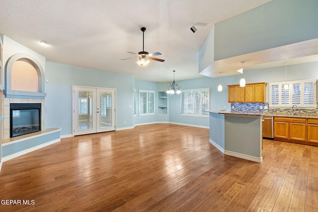 kitchen featuring a tiled fireplace, light hardwood / wood-style flooring, ceiling fan with notable chandelier, and a textured ceiling