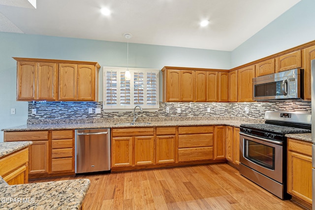 kitchen with appliances with stainless steel finishes, backsplash, light hardwood / wood-style floors, and sink