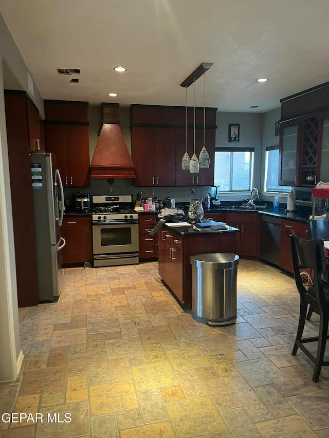 kitchen with premium range hood, sink, appliances with stainless steel finishes, decorative light fixtures, and a kitchen island