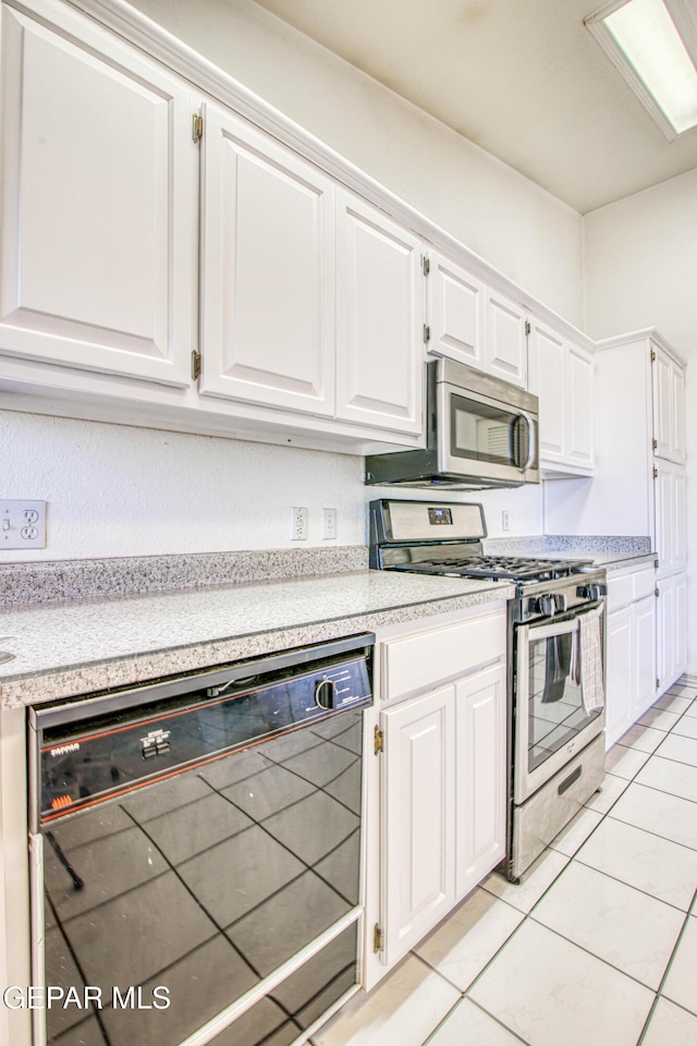 kitchen with stainless steel appliances, light tile patterned floors, and white cabinetry