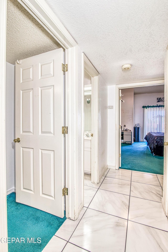 hall with a textured ceiling and light colored carpet