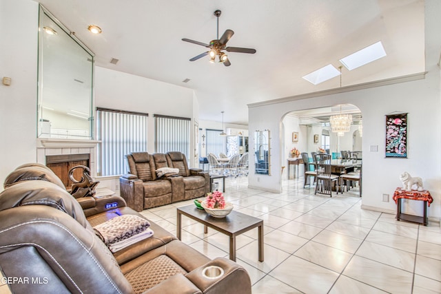 living room with ceiling fan with notable chandelier, a tiled fireplace, and lofted ceiling