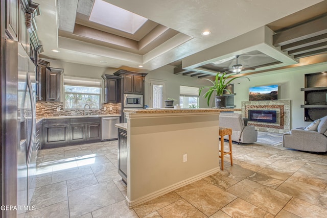 kitchen with backsplash, stainless steel appliances, a raised ceiling, ceiling fan, and a kitchen island