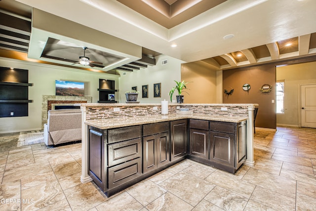 kitchen featuring ceiling fan, a spacious island, dark brown cabinetry, and light stone counters