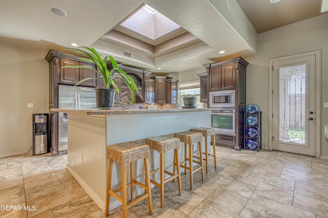 kitchen with a breakfast bar area, a skylight, dark brown cabinets, a kitchen island, and stainless steel appliances