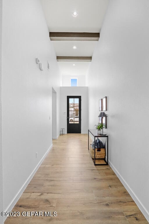 hallway featuring beam ceiling, a high ceiling, and light hardwood / wood-style flooring