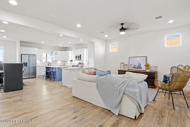 living room featuring light hardwood / wood-style flooring, ceiling fan, and a healthy amount of sunlight