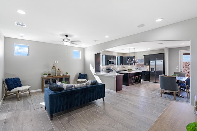 living room featuring ceiling fan, sink, a wealth of natural light, and light hardwood / wood-style flooring