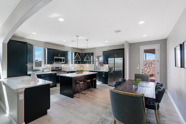 kitchen with appliances with stainless steel finishes, backsplash, a breakfast bar, decorative light fixtures, and light hardwood / wood-style floors