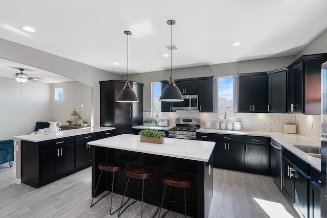 kitchen featuring ceiling fan, a center island, pendant lighting, appliances with stainless steel finishes, and light wood-type flooring