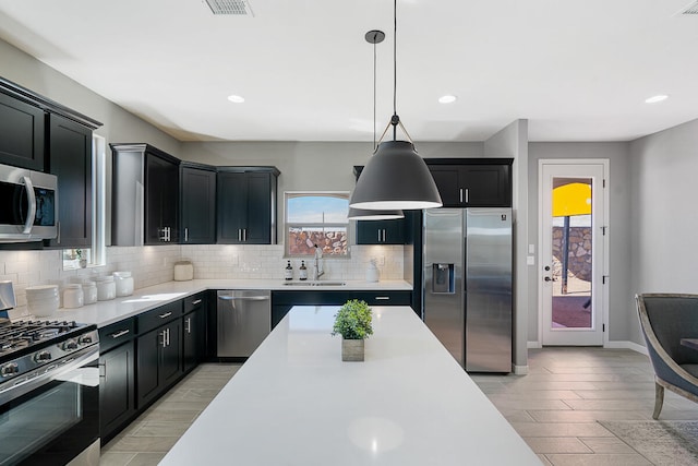 kitchen featuring pendant lighting, sink, tasteful backsplash, light hardwood / wood-style floors, and stainless steel appliances