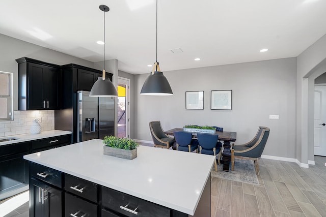 kitchen featuring stainless steel refrigerator with ice dispenser, hanging light fixtures, light hardwood / wood-style floors, tasteful backsplash, and a kitchen island