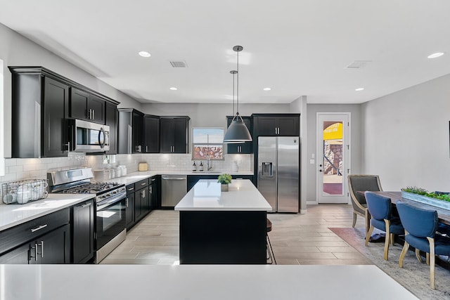 kitchen with pendant lighting, a kitchen island, stainless steel appliances, and light hardwood / wood-style flooring