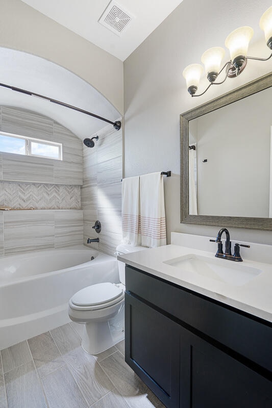 full bathroom with vanity, toilet, tiled shower / bath, and lofted ceiling