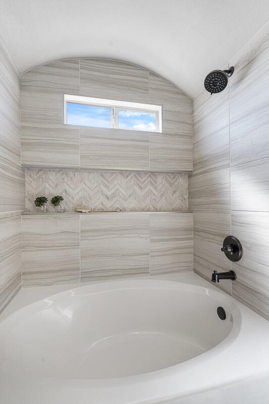 bathroom with shower / bathtub combination, a wealth of natural light, and vaulted ceiling