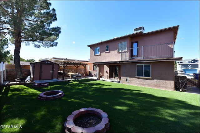 back of house featuring a balcony, an outdoor fire pit, a storage shed, and a lawn