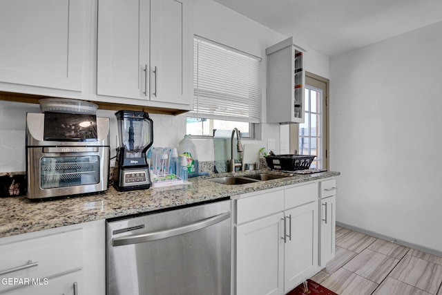 kitchen with backsplash, light stone counters, stainless steel dishwasher, sink, and white cabinetry