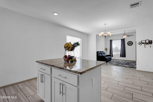 kitchen featuring white cabinets, ceiling fan with notable chandelier, dark stone countertops, decorative light fixtures, and a kitchen island