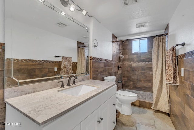 bathroom with vanity, toilet, walk in shower, and tile walls