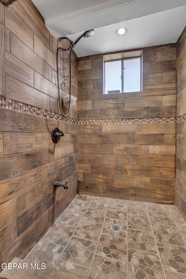 bathroom with a shower, a textured ceiling, and wooden walls