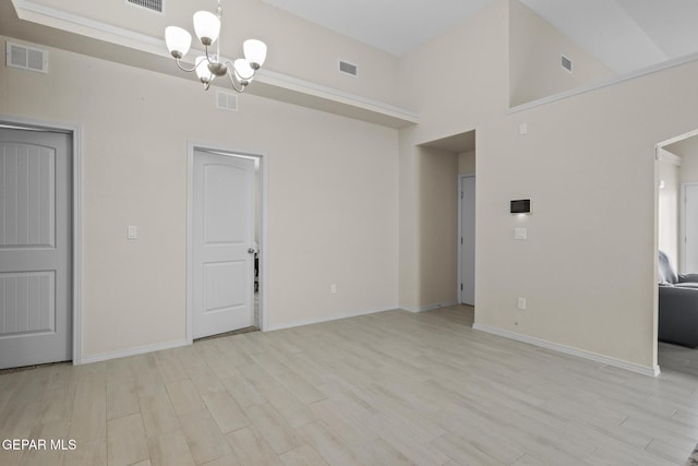 unfurnished room featuring a notable chandelier, a towering ceiling, and light hardwood / wood-style flooring