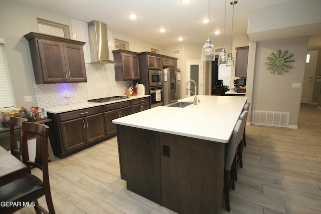 kitchen with wall chimney exhaust hood, hanging light fixtures, stainless steel appliances, a kitchen bar, and sink