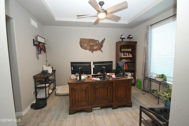 home office with light hardwood / wood-style floors, ceiling fan, a wealth of natural light, and a tray ceiling