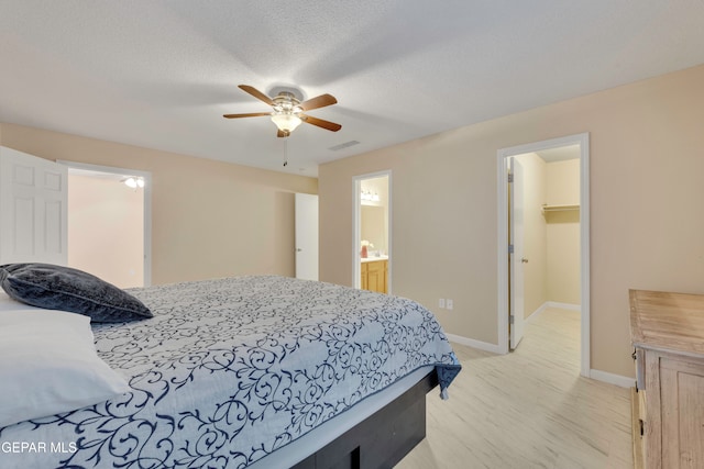 bedroom featuring connected bathroom, ceiling fan, a textured ceiling, a walk in closet, and a closet