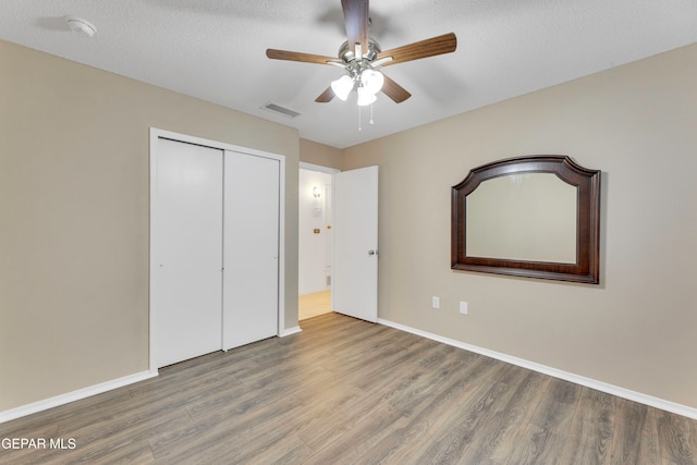 unfurnished bedroom featuring wood-type flooring, a textured ceiling, a closet, and ceiling fan