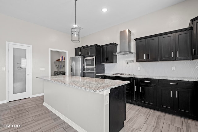 kitchen featuring tasteful backsplash, light stone counters, wall chimney exhaust hood, stainless steel appliances, and a center island