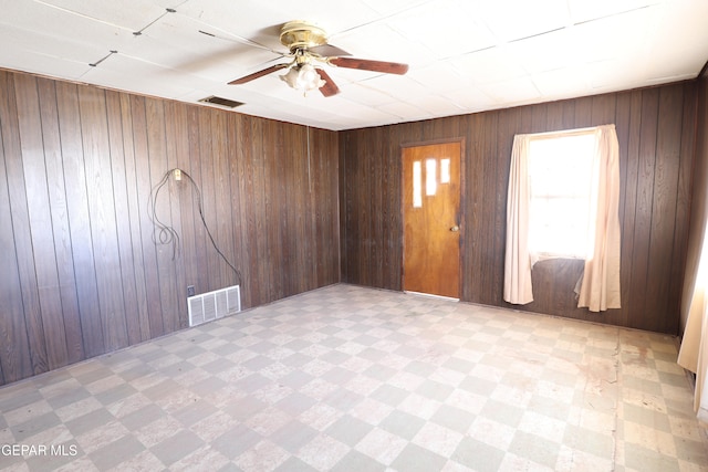 empty room featuring ceiling fan and wood walls