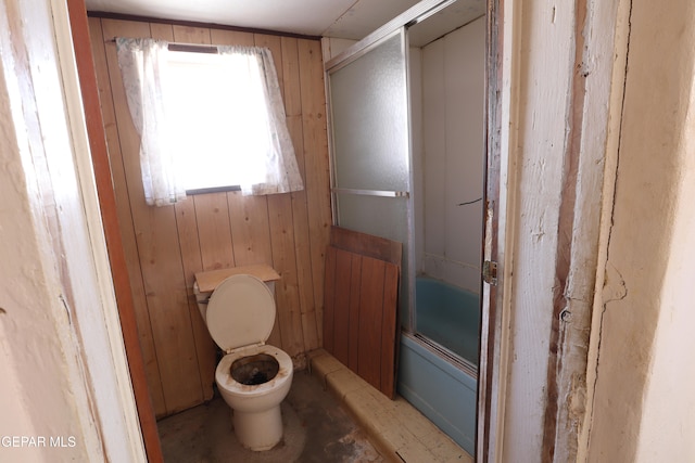 bathroom with toilet, enclosed tub / shower combo, and wooden walls