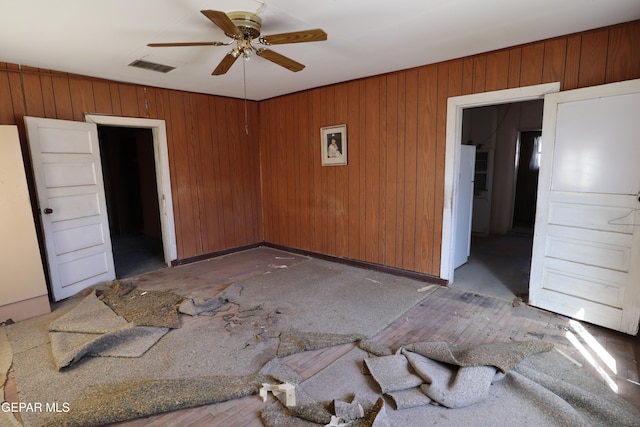 unfurnished room with ceiling fan and wooden walls