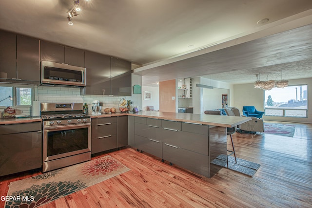 kitchen featuring light hardwood / wood-style flooring, decorative backsplash, appliances with stainless steel finishes, a kitchen bar, and kitchen peninsula