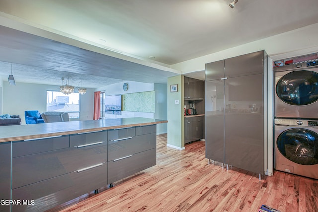 kitchen featuring a chandelier, light wood-type flooring, stacked washing maching and dryer, and gray cabinets