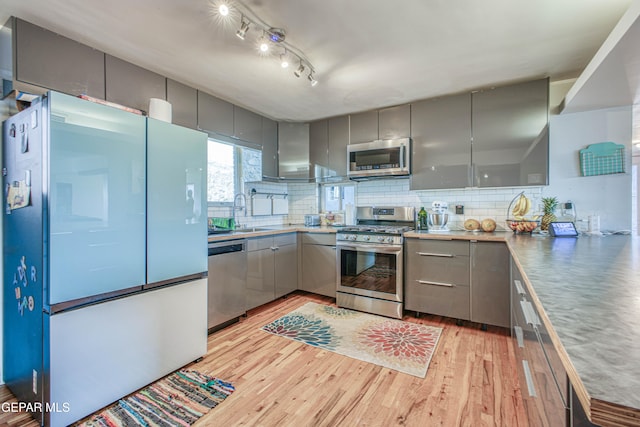 kitchen with appliances with stainless steel finishes, light wood-type flooring, backsplash, sink, and gray cabinets