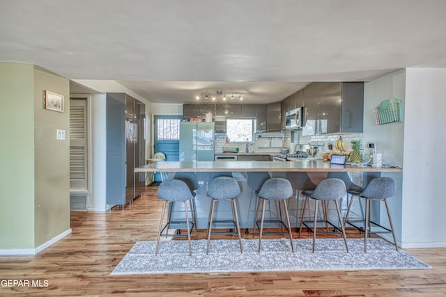 kitchen with kitchen peninsula, light wood-type flooring, tasteful backsplash, a breakfast bar, and stainless steel appliances