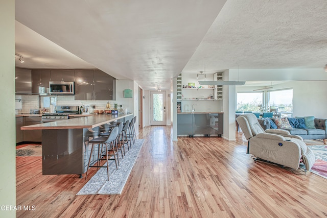 kitchen with a wealth of natural light, stainless steel appliances, light hardwood / wood-style flooring, kitchen peninsula, and a breakfast bar area