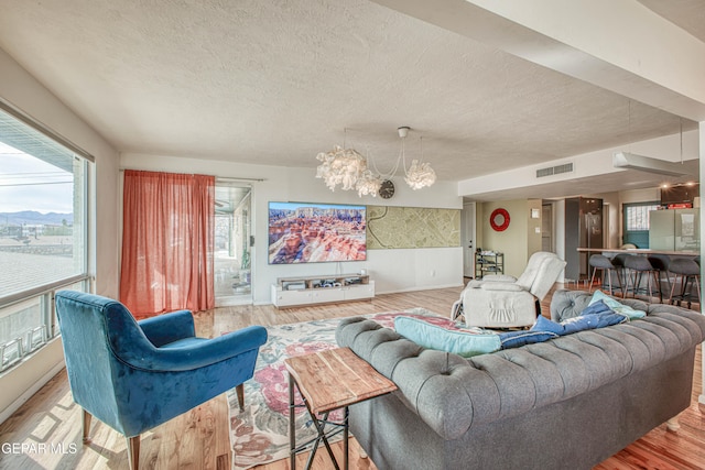 living room with light hardwood / wood-style floors, a textured ceiling, and an inviting chandelier