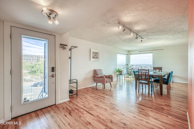 dining room with a textured ceiling, rail lighting, and light hardwood / wood-style flooring