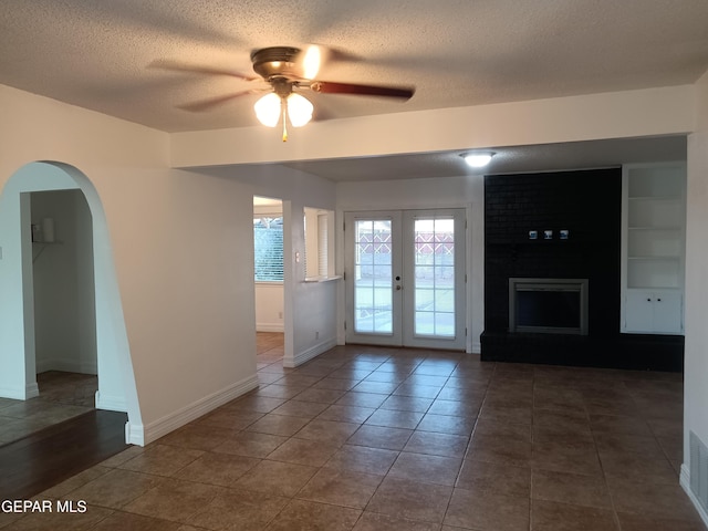 unfurnished living room with french doors, dark tile patterned flooring, ceiling fan, built in shelves, and a textured ceiling