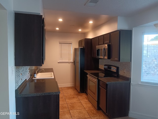 kitchen with sink, light tile patterned floors, tasteful backsplash, dark brown cabinetry, and stainless steel appliances