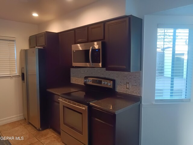 kitchen with dark brown cabinetry, stainless steel appliances, backsplash, dark stone counters, and light tile patterned flooring