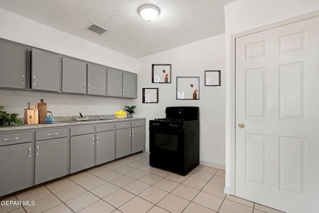 kitchen featuring sink, black gas range oven, lofted ceiling, gray cabinets, and light tile patterned flooring