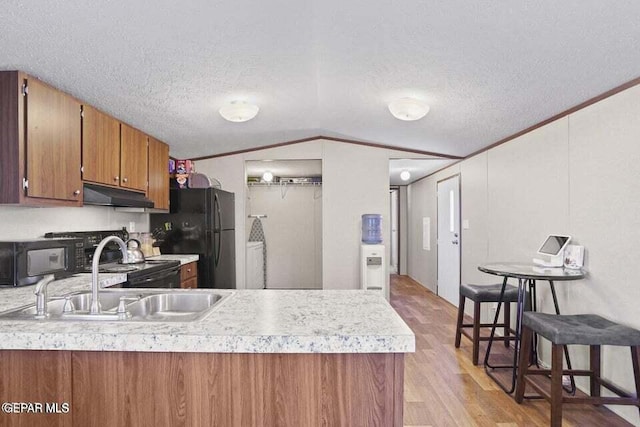 kitchen featuring a breakfast bar, lofted ceiling, black appliances, sink, and light hardwood / wood-style flooring