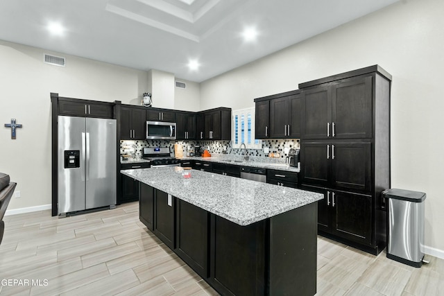 kitchen featuring sink, decorative backsplash, light stone countertops, appliances with stainless steel finishes, and a kitchen island