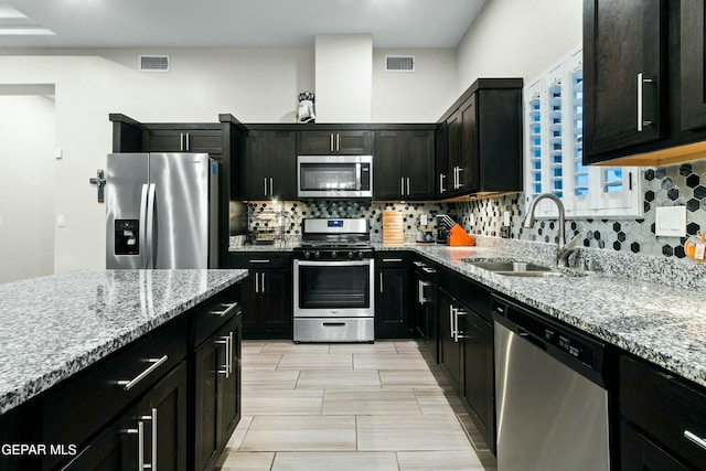 kitchen with light stone counters, sink, decorative backsplash, and stainless steel appliances