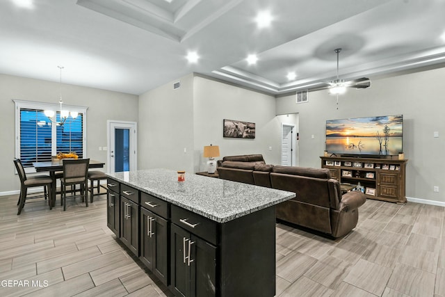 kitchen featuring light stone countertops, a kitchen island, hanging light fixtures, and ceiling fan with notable chandelier