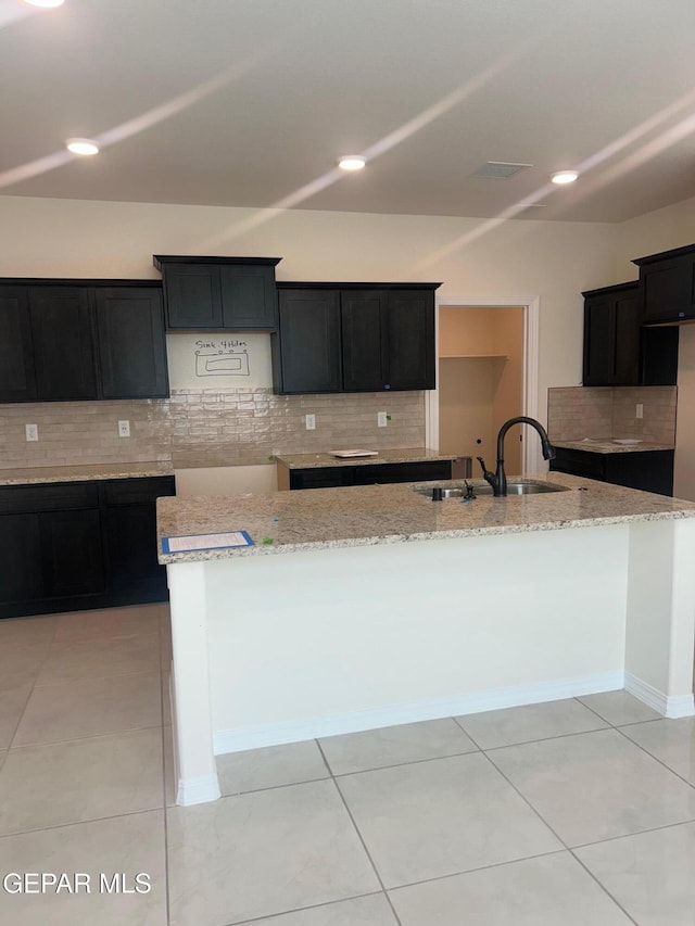 kitchen with light stone counters, sink, a center island with sink, and light tile patterned flooring